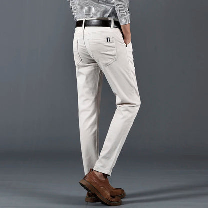Men's slim-fit white cotton dress pants with black belt, paired with striped shirt and brown leather shoes, back view.