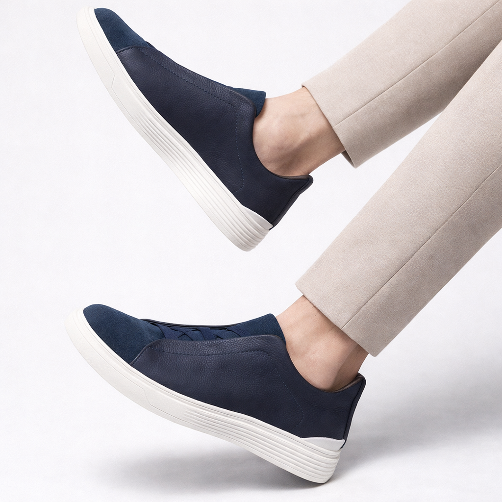 Navy blue leather and suede slip-on orthopedic sneakers with white platform sole, styled with beige trousers.