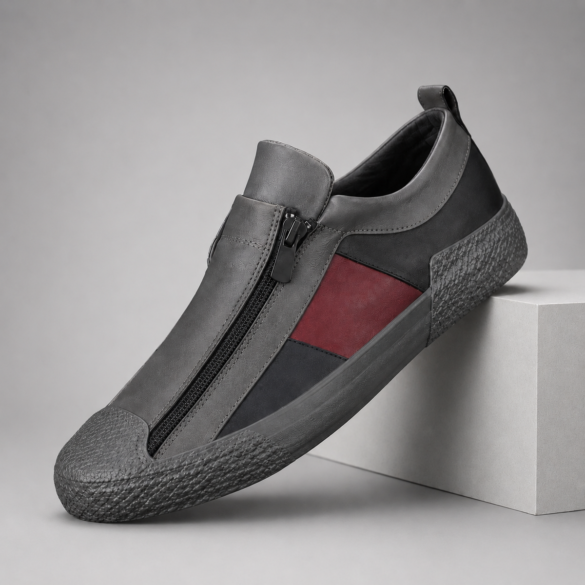 Gray leather slip-on sneakers with front zipper closure and red stripe accent on textured rubber sole