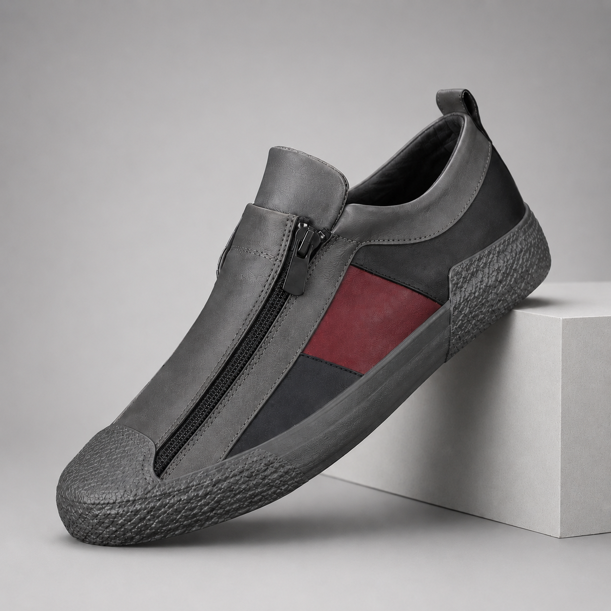 Gray leather slip-on sneakers with front zipper closure and red stripe accent on textured rubber sole