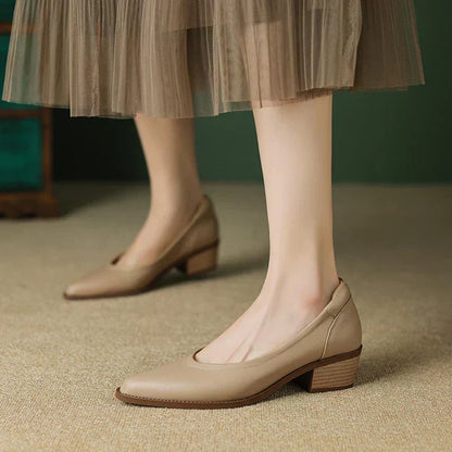 Women's beige leather pointed-toe pumps with block mid-heel, styled with a flowy mesh midi skirt on a neutral floor.