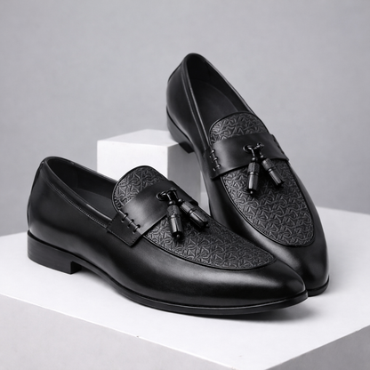 Black leather tassel loafer dress shoes for men with embossed pattern vamp detail, slip-on style, displayed on white platform.