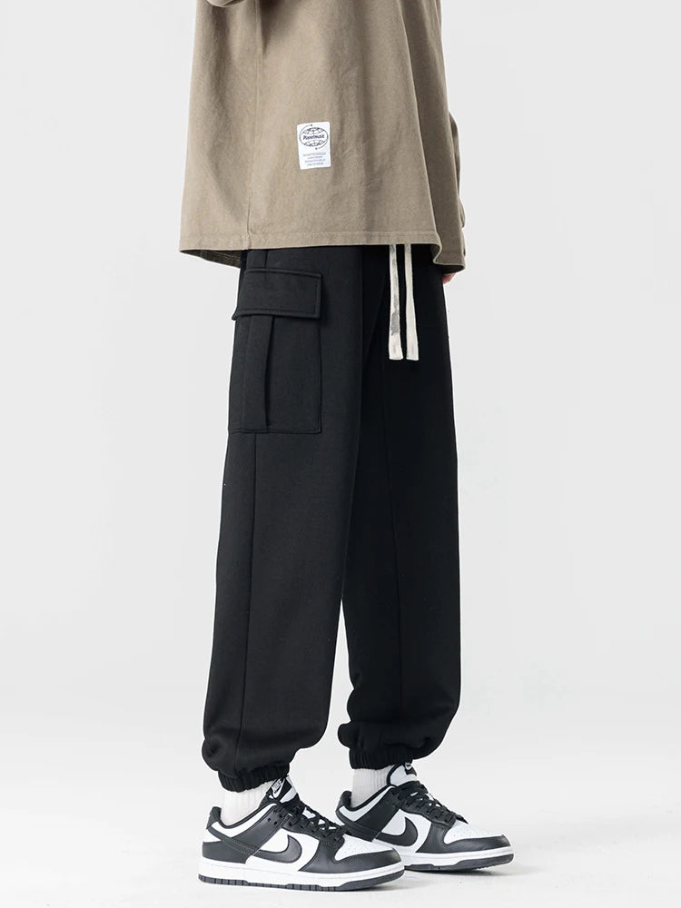 Black men's cargo jogger pants with side pockets, drawstring waist, elastic cuffs, paired with Nike sneakers.