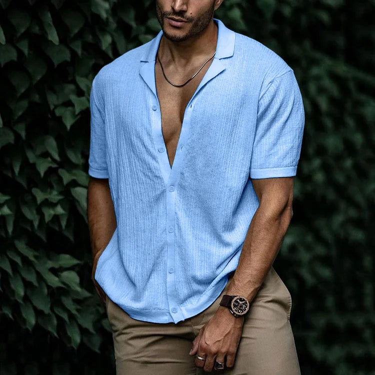 Man wearing light blue short sleeve button-down knit shirt with open collar, paired with khaki pants and a watch.