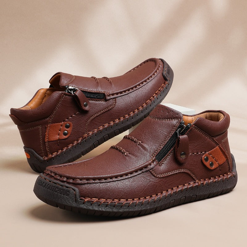Brown men's leather slip-on ankle boots with side zipper closure and hand-stitched detailing on neutral background