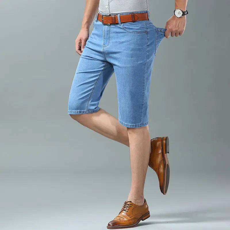Man wearing light blue stretch denim shorts with brown leather belt and tan brogue dress shoes, mid-thigh length fit.
