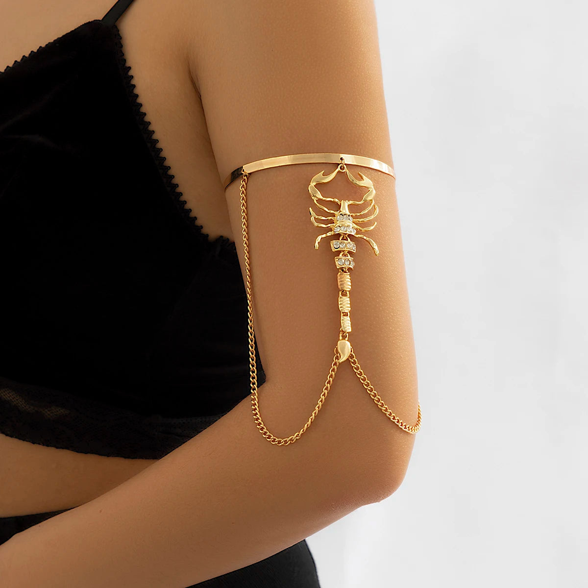 Gold scorpion upper arm cuff bracelet with crystal embellishments and chain detail worn on upper arm over black top