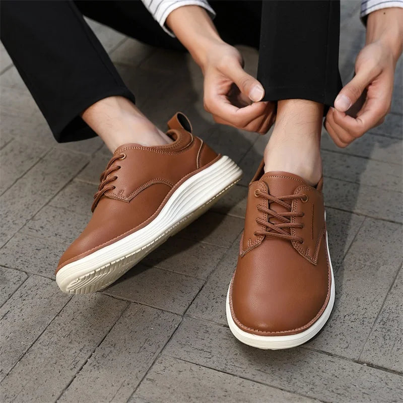 Man tying brown leather lace-up casual shoes with white soles, worn with black trousers on gray tile floor