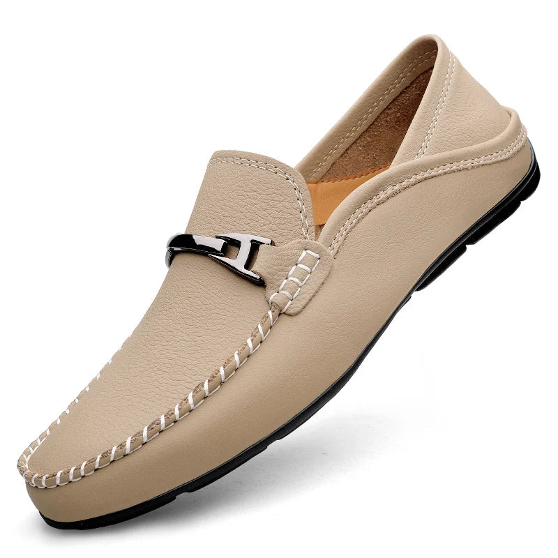 Beige men's leather slip-on loafer with silver metal H-buckle accent, white hand-stitching detail, and black sole.