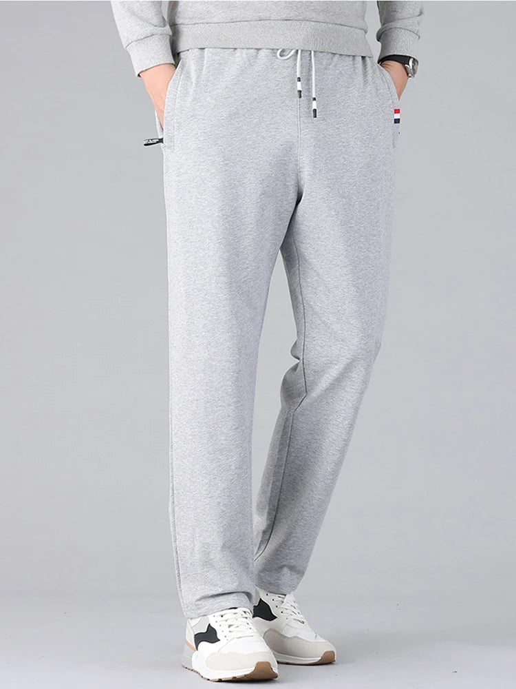 Men's light gray cotton drawstring sweatpants with side pockets, elastic waistband, and straight-leg fit, worn with white sneakers.