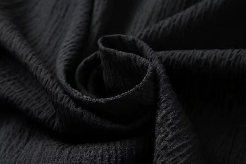 Close-up of black textured cotton linen fabric with subtle weave pattern, shown in elegant draped rose formation
