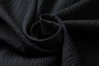 Close-up of black textured cotton linen fabric with subtle weave pattern, shown in elegant draped rose formation