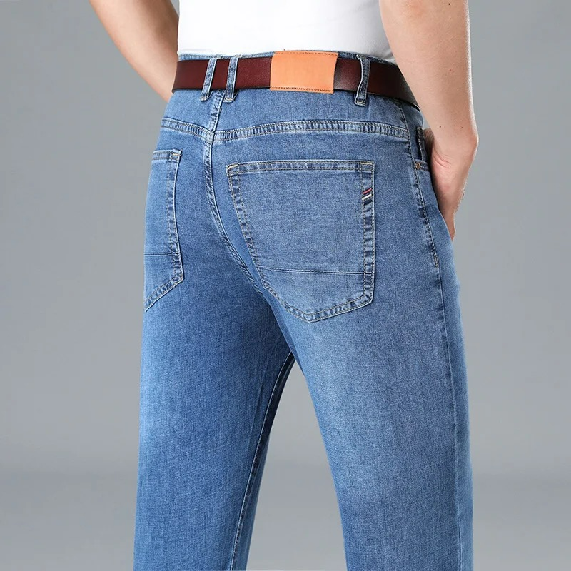 Back view of men's light blue stretch slim-fit denim jeans with brown leather belt and back pocket detail.