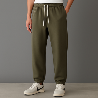 Men's olive green cotton drawstring joggers with elastic waist and cuffs, paired with white Nike sneakers.
