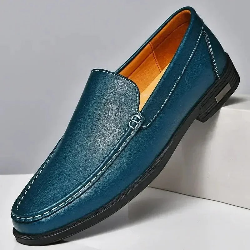 Teal blue leather men's slip-on loafer with white contrast stitching, orange interior lining, and black rubber sole.