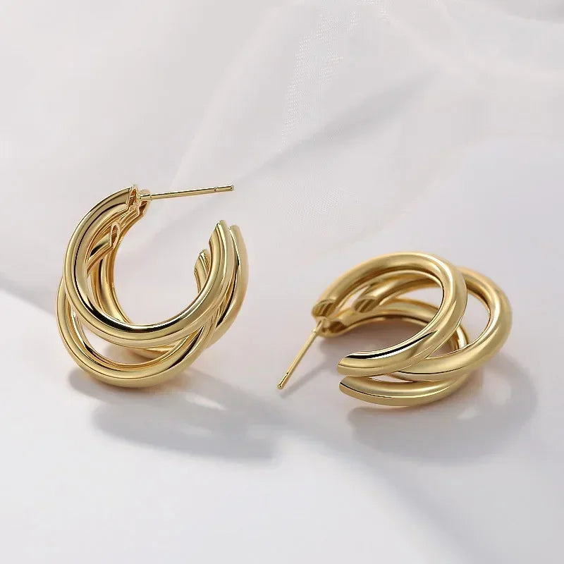 Gold triple-hoop twist earrings with snap-closure posts, shown from two angles on white fabric background.