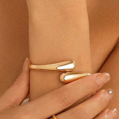 Gold tone open cuff bracelet worn on wrist, featuring sleek wrap design with tapered ends, minimalist modern style.