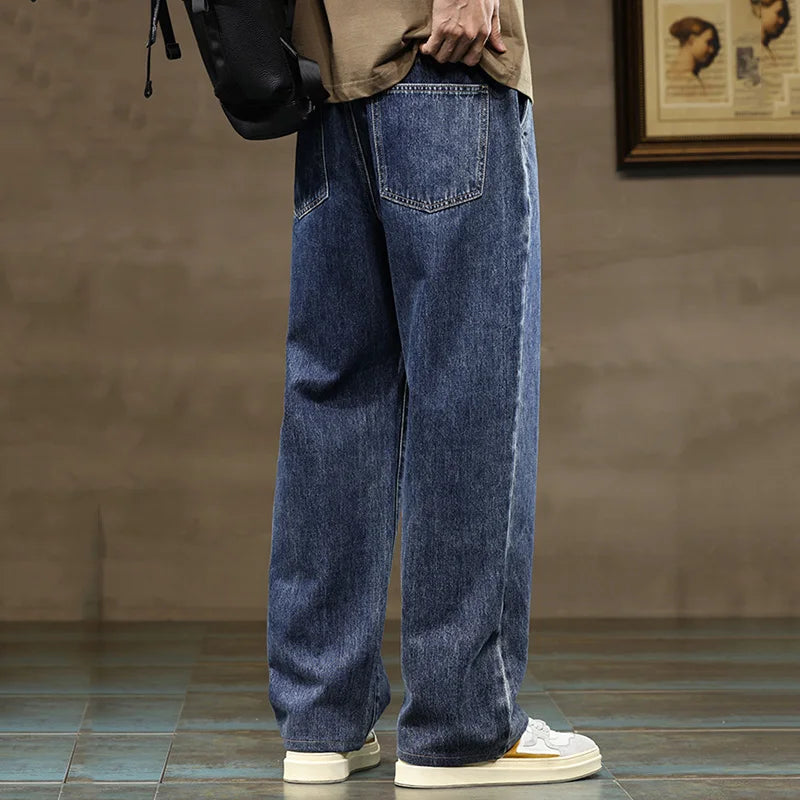 Men's wide-leg blue denim jeans with drawstring waist, worn with white sneakers and beige top, side and back view.