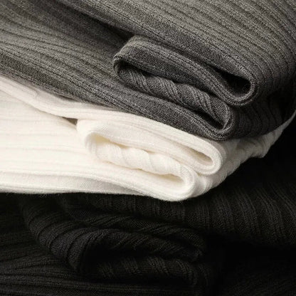 Stack of folded ribbed quarter-zip sweaters in gray, white, and black showing texture detail