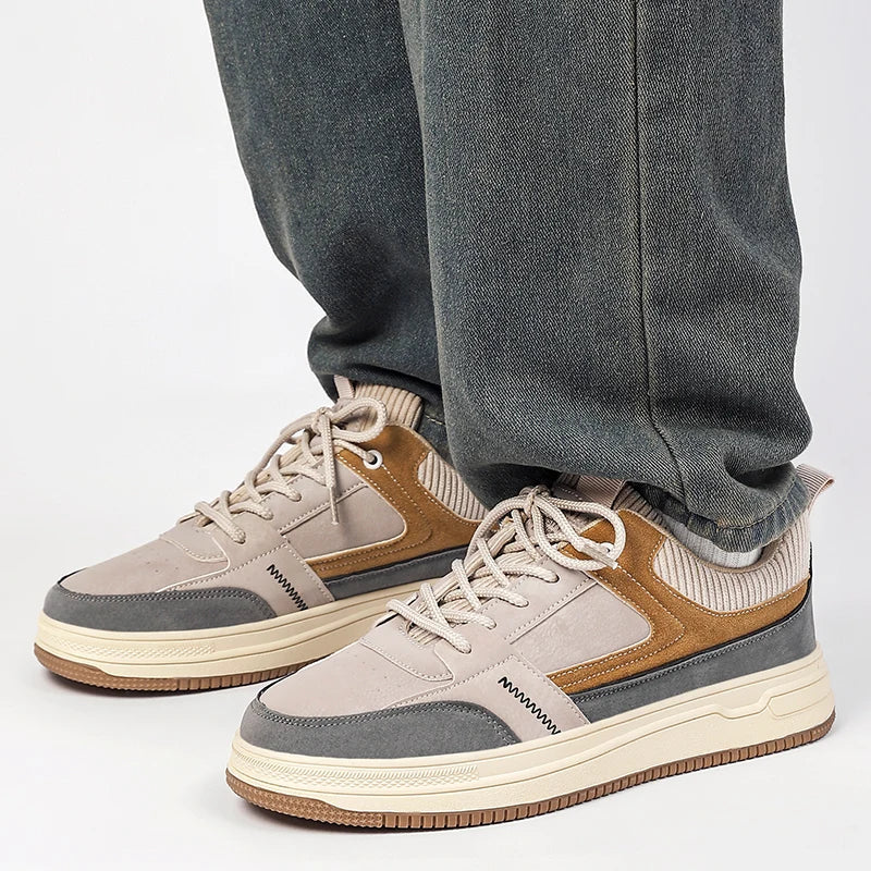 Men's patchwork low-top sneakers in beige, brown, and gray with cream sole, lace-up style, worn with gray jeans.