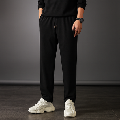 Man wearing black ice silk drawstring sweatpants with white sneakers and black long sleeve top, casual athletic style.