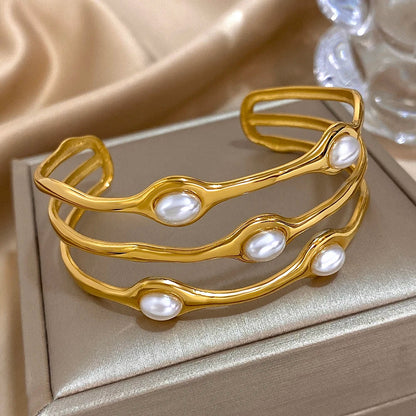 Gold tone open cuff bangle bracelet with three wavy rows and oval pearl accents, displayed on a jewelry box.
