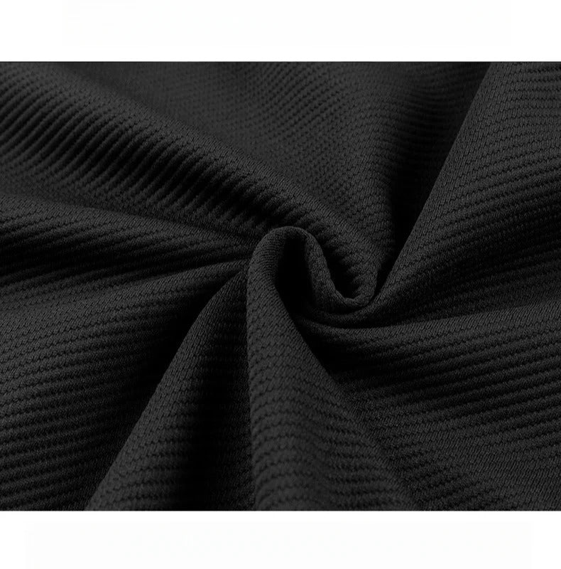 Close-up of black textured ribbed fabric with subtle waffle knit pattern, draped in soft folds showing fabric quality.