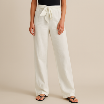 Women's white linen wide-leg pants with tie waist, paired with black flip flops and black top, neutral background.