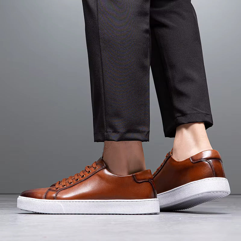 Men's tan leather lace-up sneakers with white rubber sole, paired with dark dress trousers on gray background.
