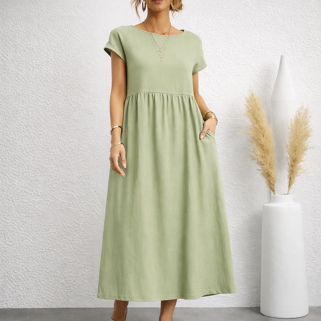 Woman wearing a sage green short-sleeve relaxed linen midi dress with empire waist, gathered skirt, and side pockets