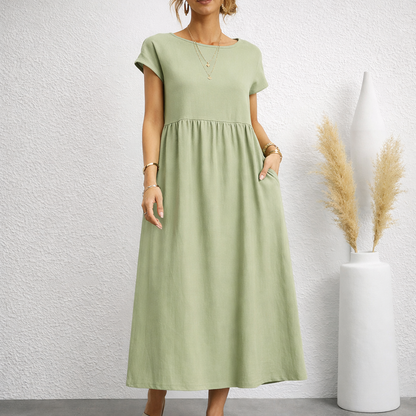 Woman wearing a sage green short-sleeve relaxed linen midi dress with empire waist, gathered skirt, and side pockets