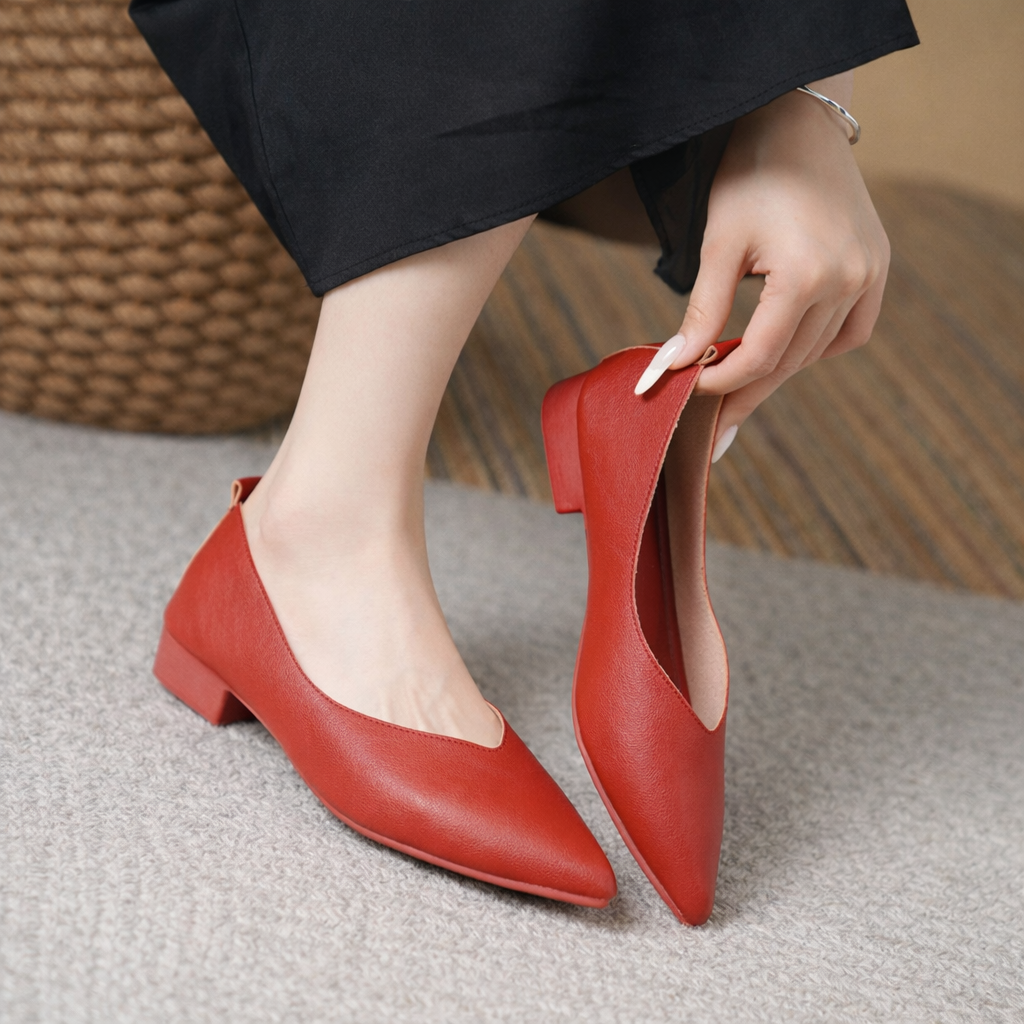 Red leather block heel pumps with pointed toe, worn by woman in black pants, shown being put on foot.