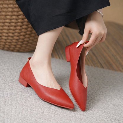 Red leather block heel pumps with pointed toe, worn by woman in black pants, shown being put on foot.
