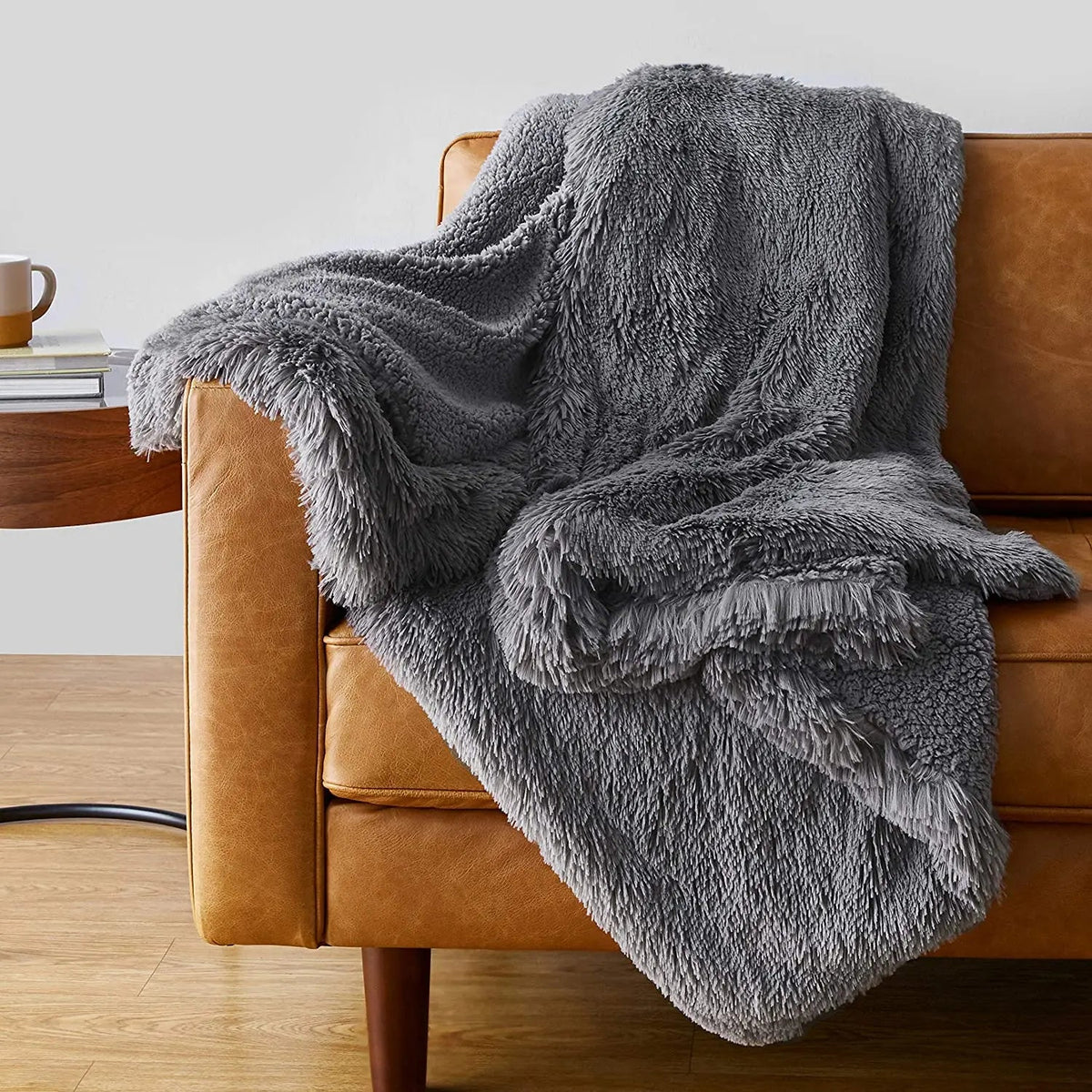 Gray faux fur plush throw blanket draped over tan leather armchair with wood side table