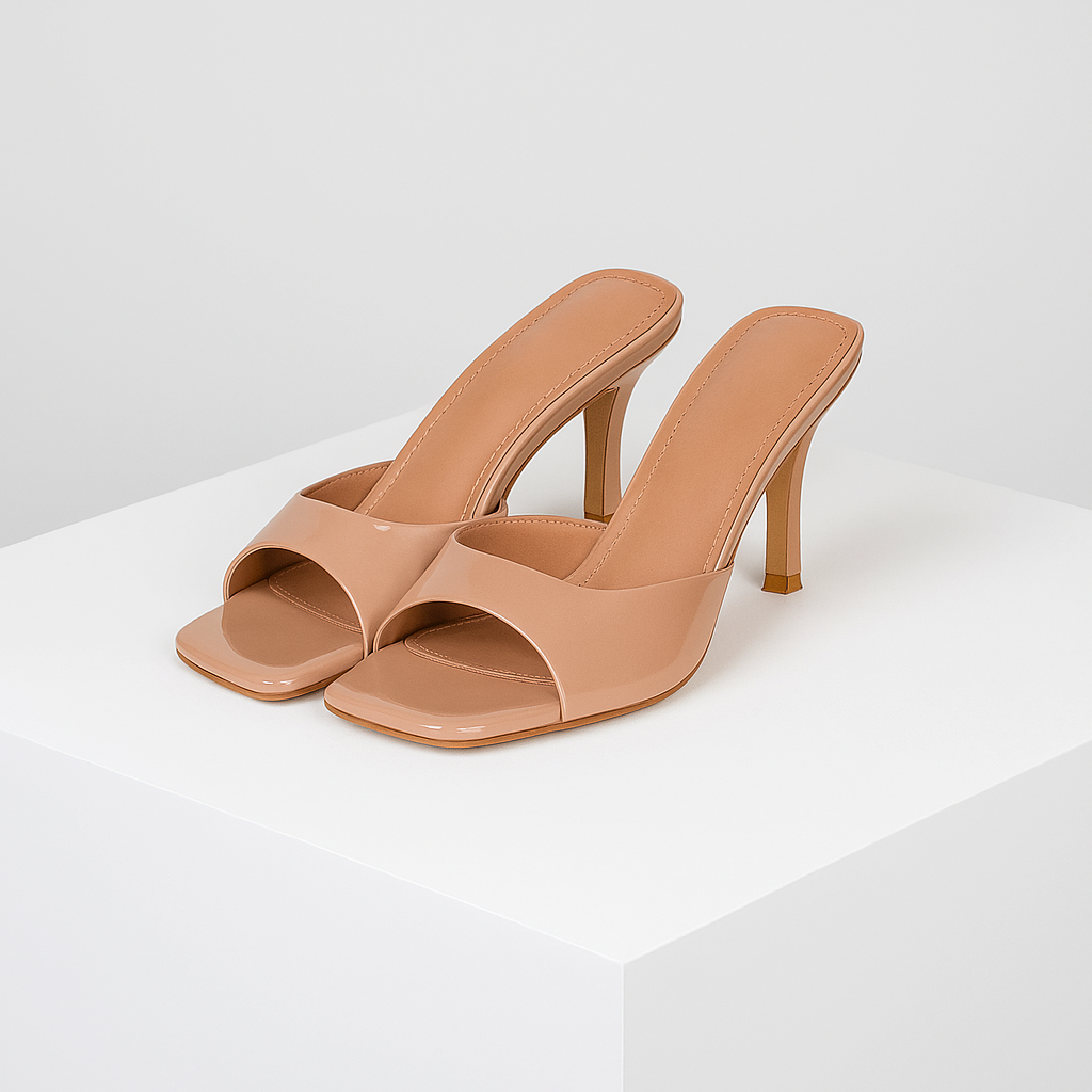 Nude patent leather square-toe mule heels with slim stiletto heel displayed on white pedestal