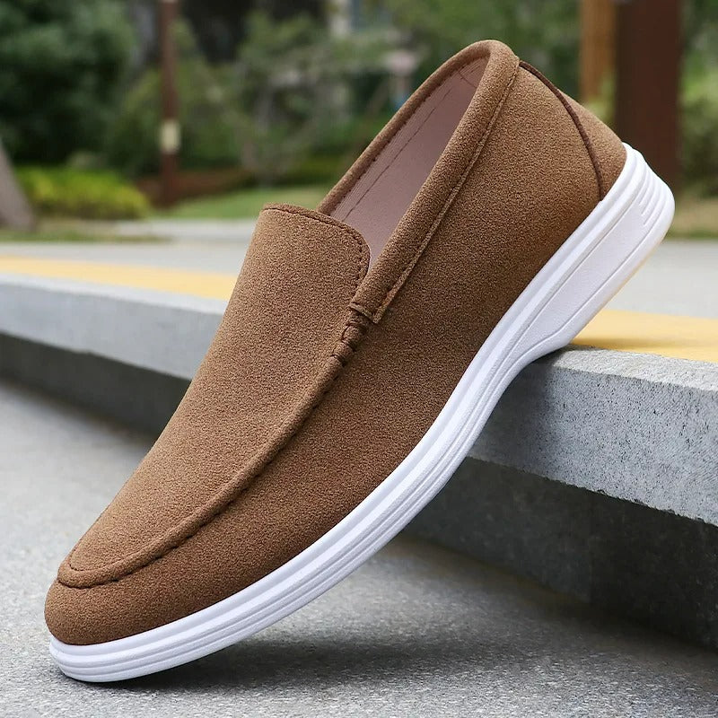 Brown suede slip-on loafers with white rubber sole displayed on concrete steps outdoors