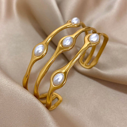 Gold tone pearl cuff bracelet with organic wave design and white baroque pearls on beige silk fabric