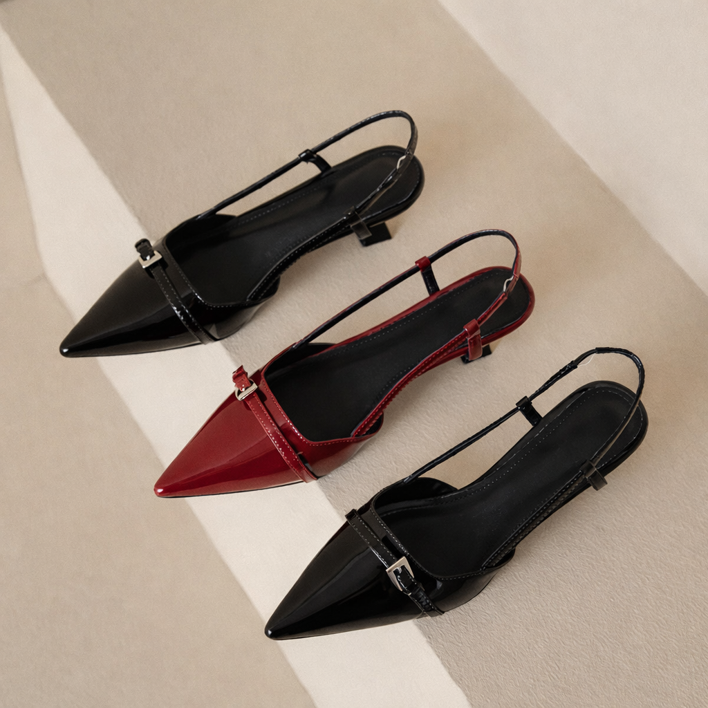 Three patent leather pointed-toe slingback heels with buckle detail in black and burgundy red colorways displayed on beige surface.