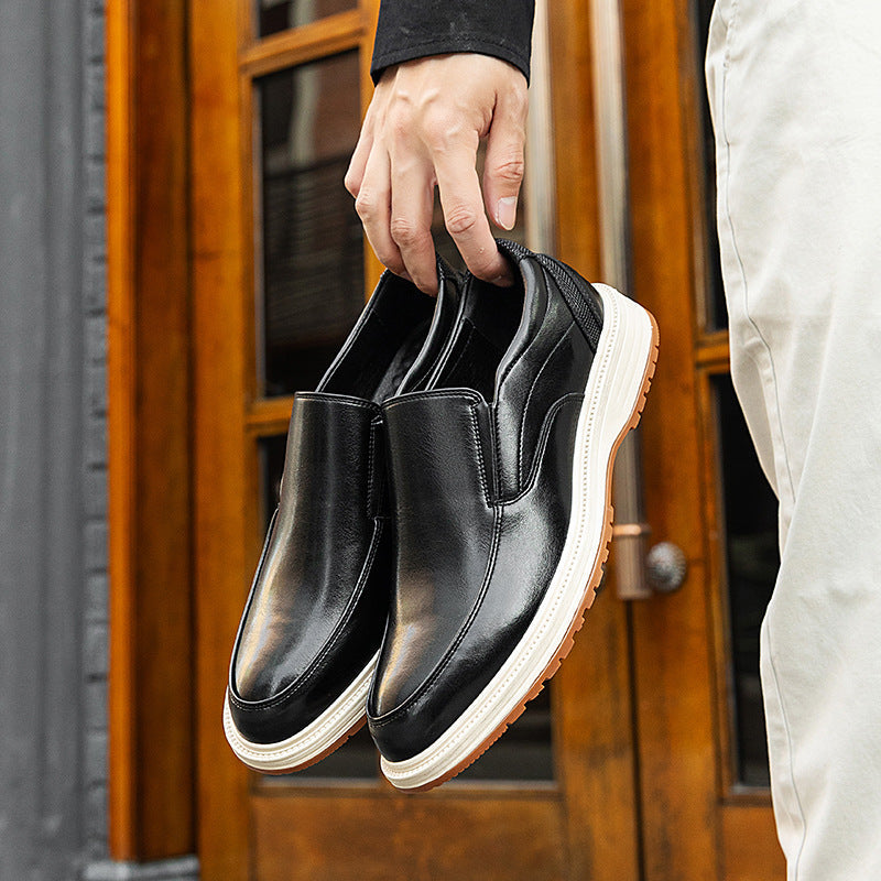 Man holding black leather slip-on loafers with white platform sole and tan outsole against wooden door backdrop
