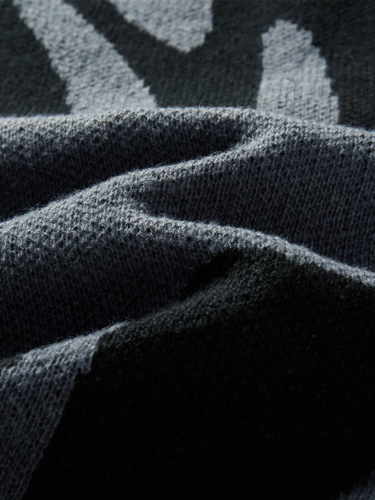 Close-up of dark charcoal wool knit fabric with grey abstract geometric pattern, showing soft textured weave detail