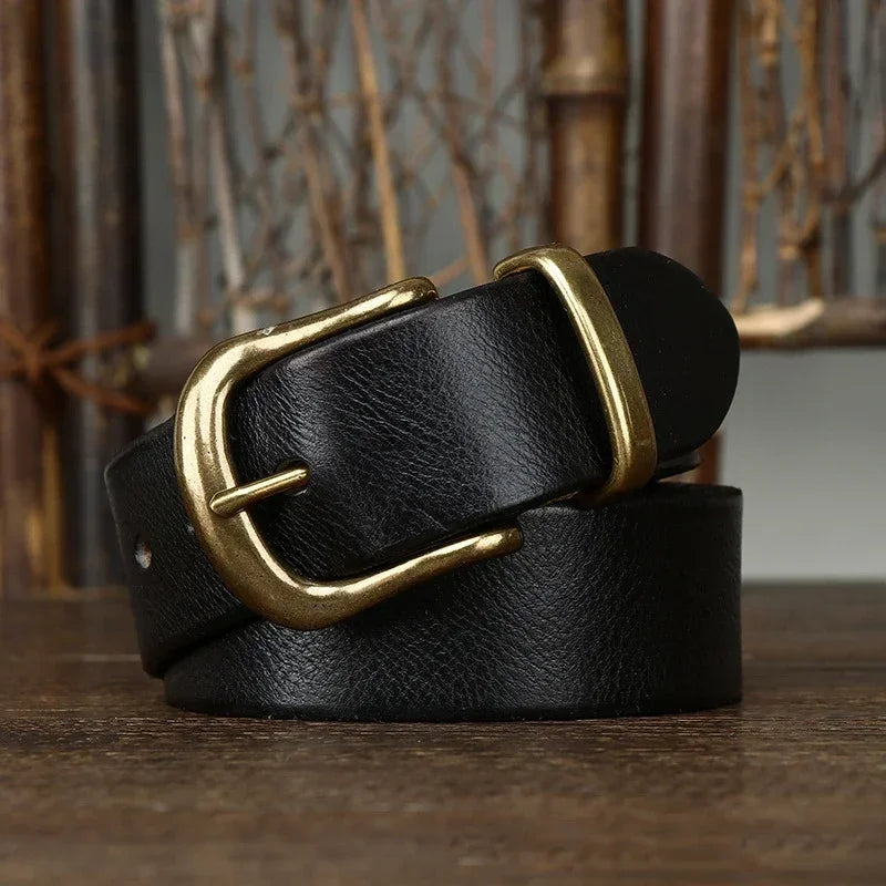 Black leather men's belt coiled on wood surface, featuring an antique brass pin buckle, rustic background