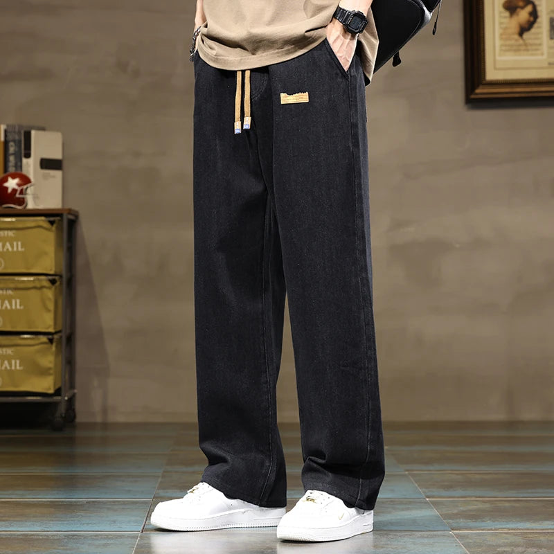 Man wearing black wide-leg drawstring denim jeans with tan top and white sneakers, casual streetwear style