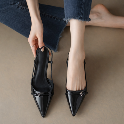 Black patent leather pointed-toe slingback heels with buckle detail, shown being worn with cropped blue jeans.