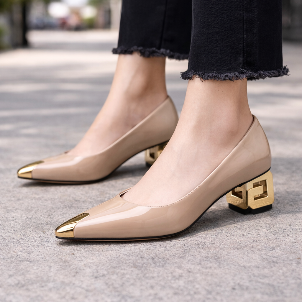 Nude patent leather block heel pumps with gold toe cap and decorative geometric heel, worn with black frayed jeans.