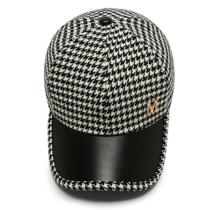 Black and white houndstooth baseball cap with black leather brim and gold M logo emblem, structured fit