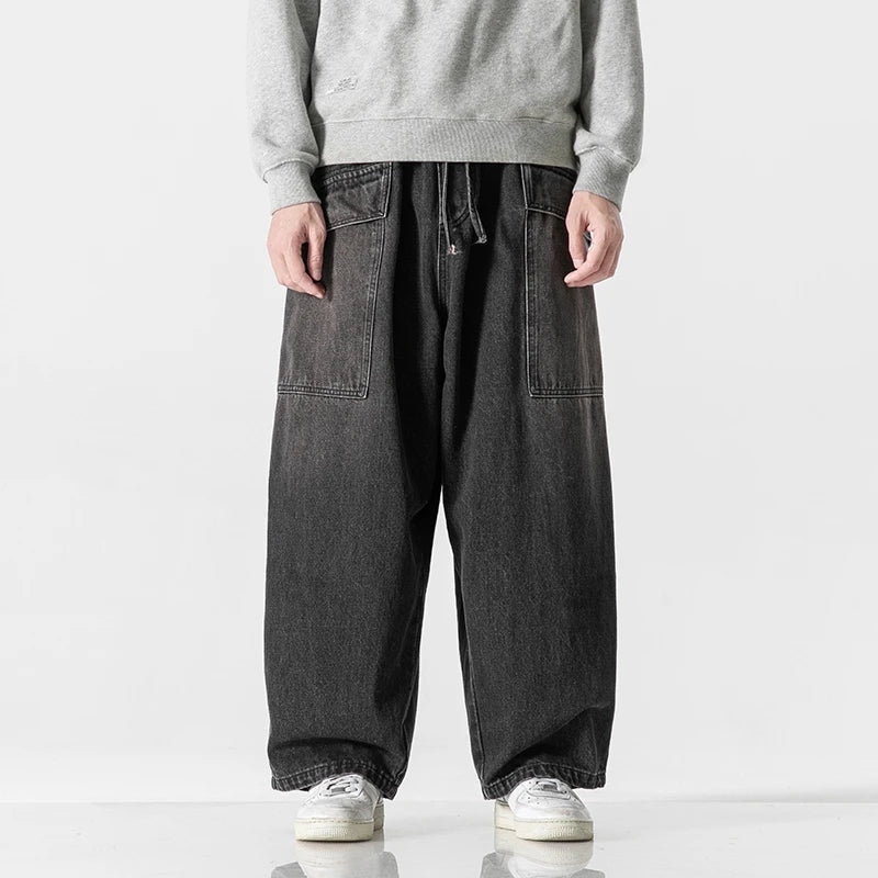 Men's wide-leg black washed denim jeans with large patch pockets and drawstring waist, paired with white sneakers