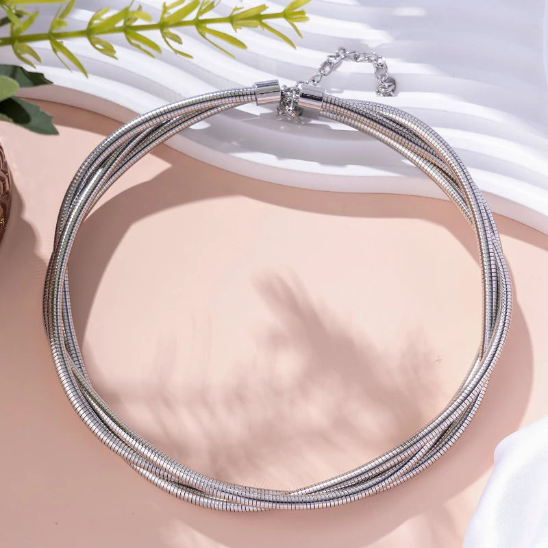 Silver multi-strand snake chain choker necklace with barrel clasp and safety chain extension displayed on pink surface