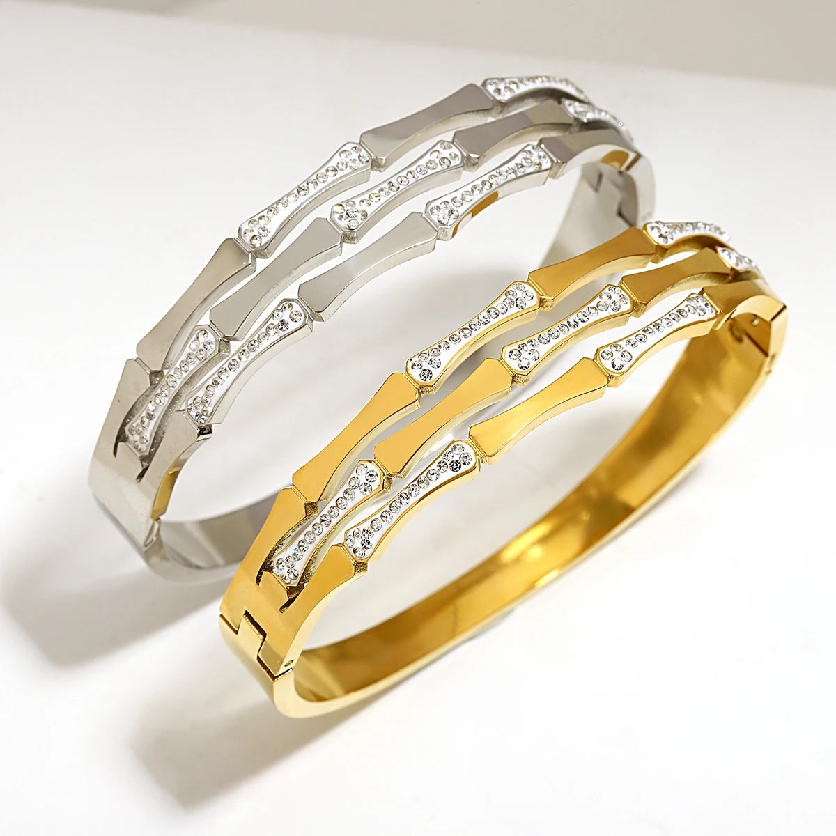 Two geometric bangle bracelets in gold and silver tones with crystal stone accents in angular segmented design