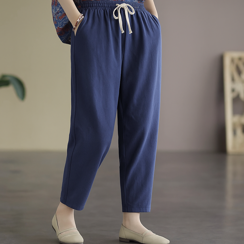 Women's blue linen drawstring tapered pants with elastic waist, side pockets, cropped length, paired with flat loafers.