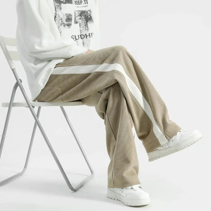 Men's wide-leg khaki corduroy joggers with white side stripes, paired with white sneakers and graphic sweatshirt.
